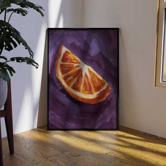 Framed artwork of a sliced orange on a purple background in a room with wooden floor and plant.