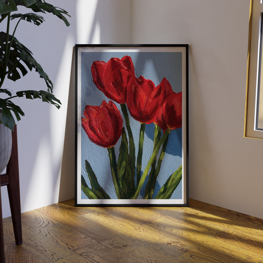 Framed painting of red tulips on a wall with a plant and wooden floor.